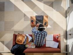 aerial photo of student sitting on couch, wearing headphones and working on computer